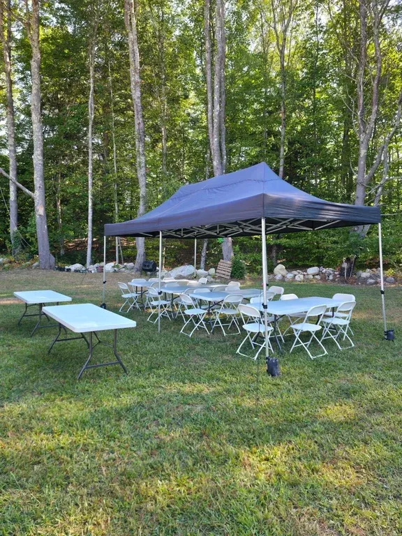 Black pop-up tent with white folding tables and chairs set up in a grassy backyard for a bachelor party.