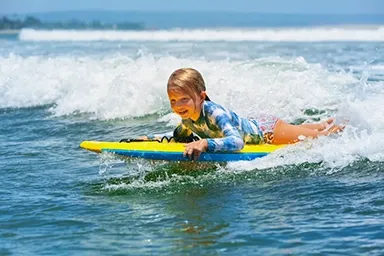 Kids having fun with a bodyboard in the waves at an Ulladulla beach.